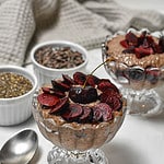 chocolate cherry pudding in a bowl with little bowls filled with chia seeds and cacao nibs behind it