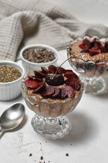 chocolate cherry pudding in a bowl with little bowls filled with chia seeds and cacao nibs behind it