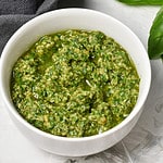 Walnut Pesto with Lemon in a white bowl, with grey napkin and basil in the back