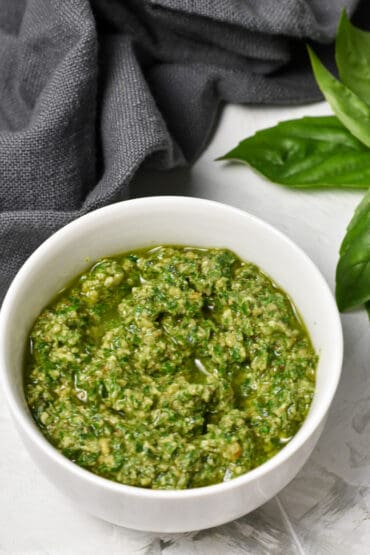 Walnut Pesto with Lemon in a white bowl, with grey napkin and basil in the back