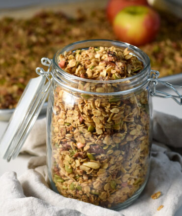 Healthy Apple cinnamon granola in a jar, with oats and apples in the background