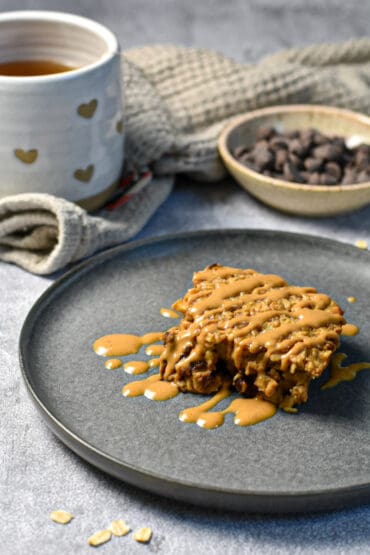 Healthy Chocolate Peanut Butter Baked Oatmeal drizzled with peanut butter, tea and chocolate chips in the background