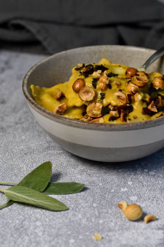 Creamy pumpkin pasta with toasted hazelnuts and sage in a bowl, with hazelnuts and sage sprinkled in the front