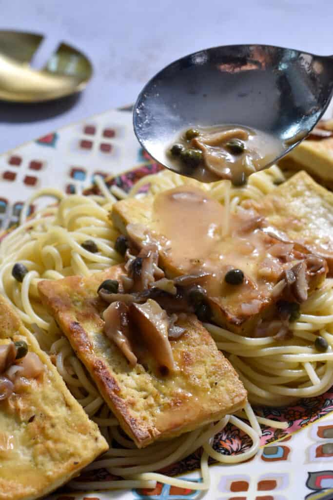 Easy Tofu Piccata [with lemon and capers] on a platter with sauce being spooned over