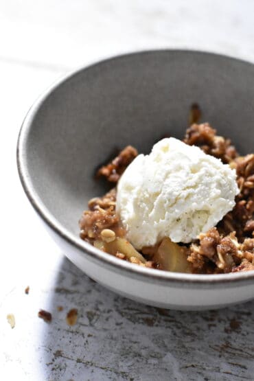 Cardamom Apple Crumble topped with vanilla bean ice cream in a grey bowl