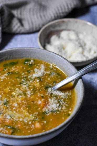 Creamy Lemon Chickpea Potato Soup in a bowl with a bowl of parmesan behind it.