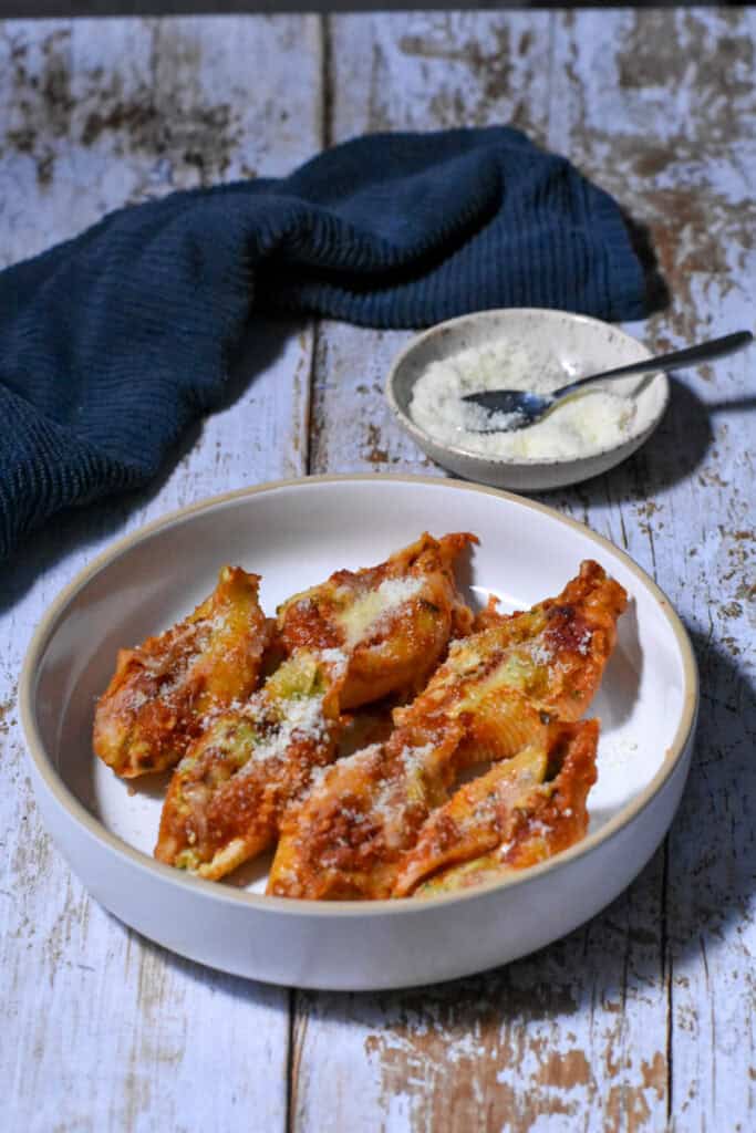 Healthy Srtuffed Shells in a bowl with a bowl of grated cheese, and a blue napkin in the back