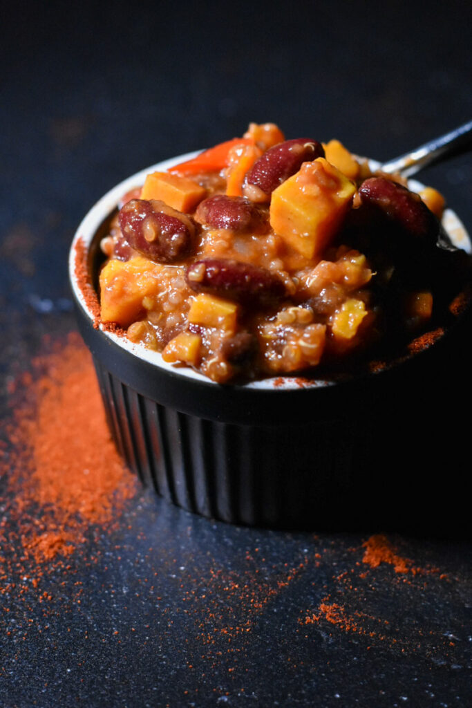 Sweet Potato Quinoa Chili in a black bowl, with spices sprinkled in the front