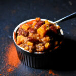 Sweet Potato Quinoa Chili in a black bowl, with spices sprinkled in the front