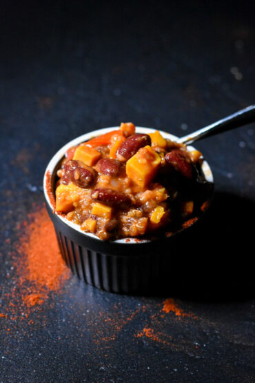 Sweet Potato Quinoa Chili in a black bowl, with spices sprinkled in the front