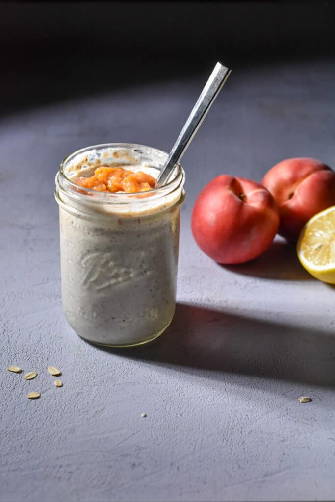 Peach pie overnight oats in a mason jar with peaches and a lemon in the background