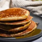 stack of fluffy banana oat pancakes wiht syrup dripping off and with a tan napkin in the background