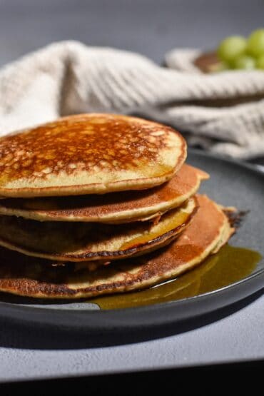 stack of fluffy banana oat pancakes wiht syrup dripping off and with a tan napkin in the background