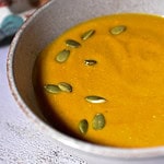 Creamy butternut squash soup topped with pumpkin seeds in a rustic bowl. Perfect comfort food for gatherings and fall seasons.