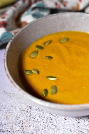 Creamy butternut squash soup topped with pumpkin seeds in a rustic bowl. Perfect comfort food for gatherings and fall seasons.