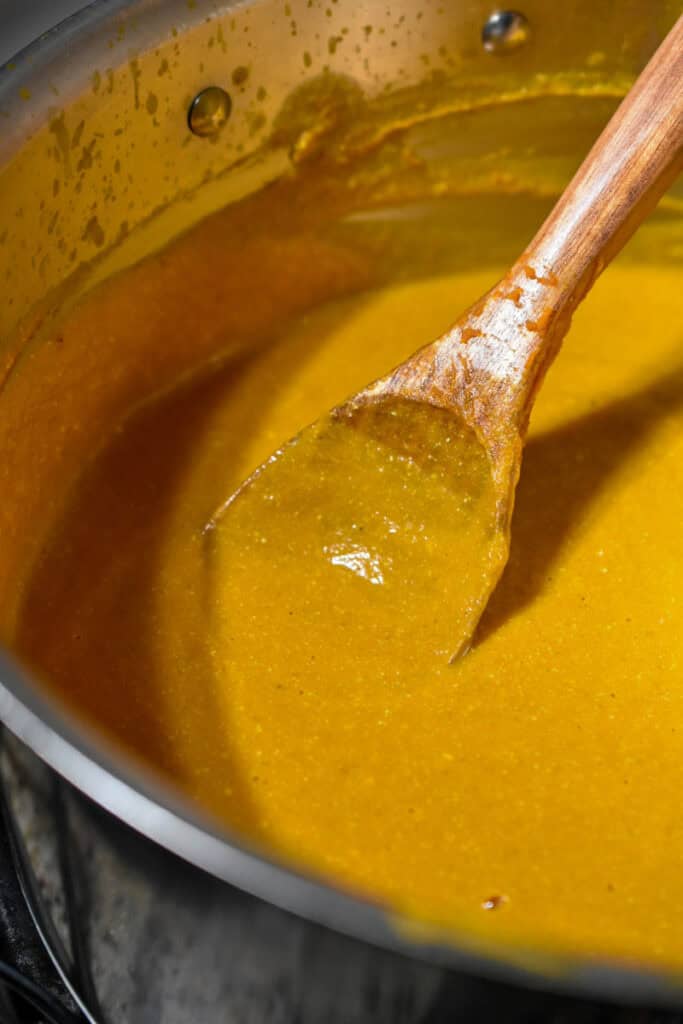 Savory yellow curry in a stainless steel pot with wooden spoon, ready for serving.
