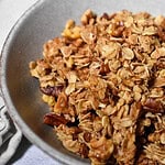 Maple Pecan Granola in a grey bowl with a beige napkin in the back