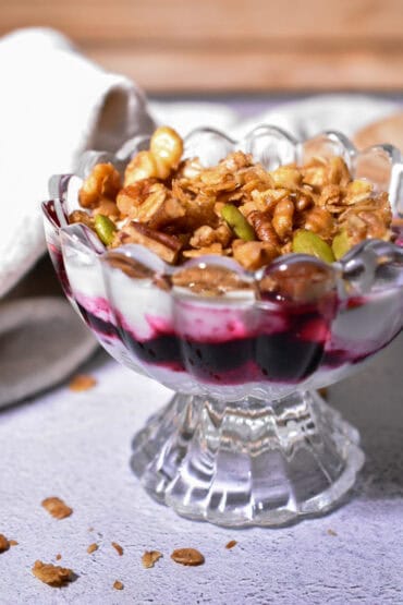 Pecan Maple Granola sprinkled over a yogurt parfait in a scalloped glass