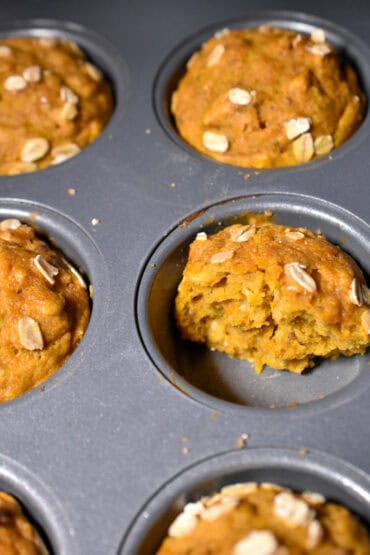 pumpkin oat muffins in a muffin tin. One cut in half