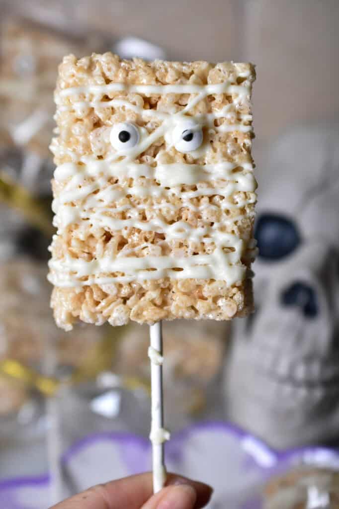 Homemade mummy Rice Krispie treats decorated with white chocolate bandages and candy eyes for Halloween