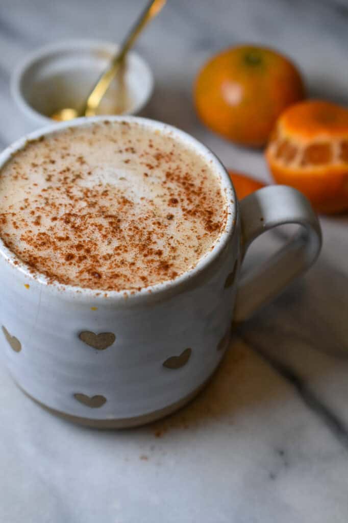 orange honey cardamom latte with an orange and cup with a gold spoon in the background